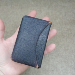 May include: A small, black leather card case with a rounded corner. The case is slightly worn and has a textured surface.