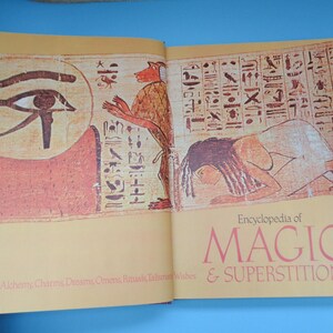 May include: An open book titled "Encyclopedia of Magic & Superstition" with illustrations of an Egyptian eye and a woman lying down. The book cover is yellow with red and black text.