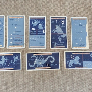 May include: A set of ten vintage cards featuring constellations with blue and white illustrations and text. The cards are printed on white cardstock with red and black borders. The constellations include: Great Bear, Algol, Crab, Twins, Bull, Auriga, Little Bear, Archer, Scorpion, and Lion.