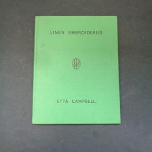 May include: A green book titled "LINEN EMBROIDERIES" by Etta Campbell. The book cover has a simple design with the title and author's name in black text. A small, circular emblem is centered on the cover.