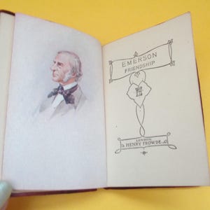 May include: Open miniature book with a maroon cover. The left page features a watercolor portrait of a man with white hair and a bow tie. The right page displays the title "EMERSON FRIENDSHIP" and the publisher's name.