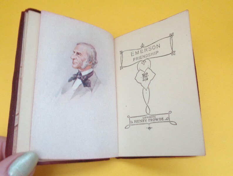 May include: Open miniature book with a maroon cover. The left page features a watercolor portrait of a man with white hair and a bow tie. The right page displays the title "EMERSON FRIENDSHIP" and the publisher's name.