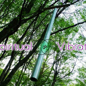 May include: A silver metal tube hanging from a tree branch in a forest. The tube is surrounded by green leaves and the text "Spiritual Vibrations" is superimposed on the image.