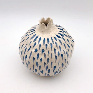 Op de afbeelding: Witte keramische vaas in de vorm van een granaatappel met een abstract blauw en wit patroon.