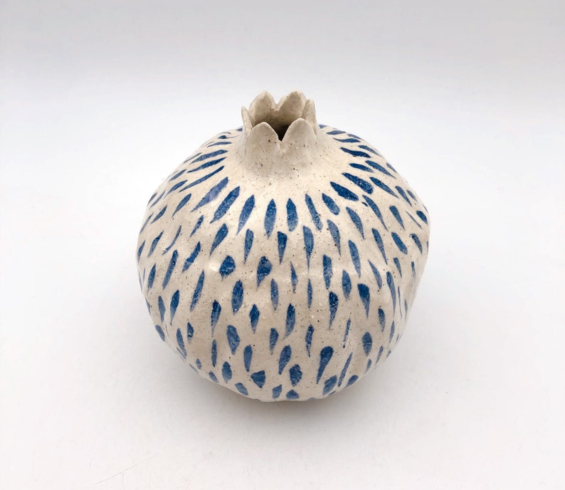 Op de afbeelding: Witte keramische vaas in de vorm van een granaatappel met een abstract blauw en wit patroon.