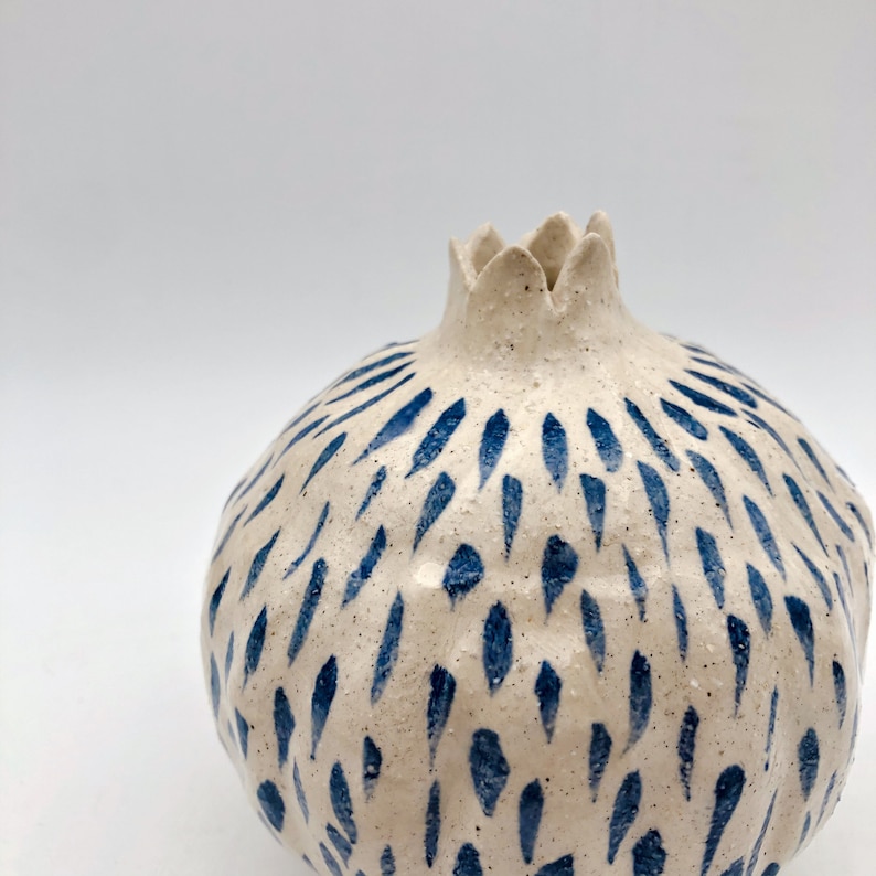 Op de afbeelding: Een witte keramische vaas in de vorm van een granaatappel met een abstract blauw en wit patroon.