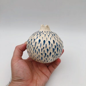 Op de afbeelding: Witte keramische vaas in de vorm van een granaatappel met een abstract blauw en wit patroon.