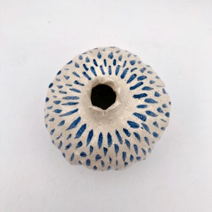 Op de afbeelding: Een witte keramische vaas met een abstract blauw en wit patroon. De vaas heeft een brede opening en een ronde bodem.