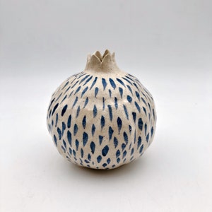 Op de afbeelding: Witte keramische vaas in de vorm van een granaatappel met een blauw en wit gespikkeld patroon.