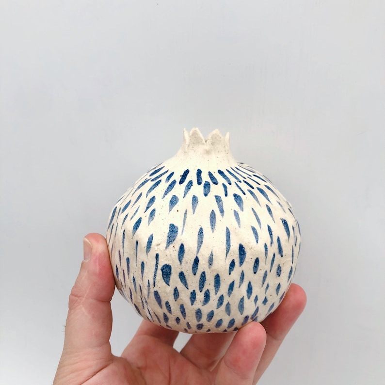 Op de afbeelding: Een witte keramische vaas in de vorm van een granaatappel met een abstract blauw en wit patroon.