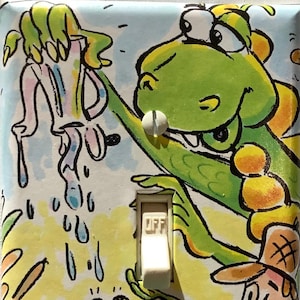 May include: A light switch cover with a colorful cartoon design featuring a green dinosaur, a frog playing a saxophone, and a person with a hat. The switch is labeled "OFF".