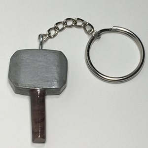 May include: A silver and brown metal keychain shaped like a hammer. The hammer has a round head and a long, thin handle.