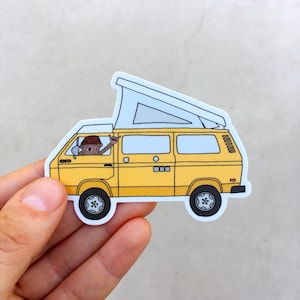May include: A yellow camper van with a pop-up roof and a bear wearing a hat in the driver's seat waving. The van has a white roof and black trim.