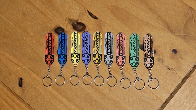 May include: A collection of keychains in various colors, including red, blue, yellow, and green. Each keychain features a rectangular design with the word "ASOSOKO" and a circular emblem, attached to a silver keyring.