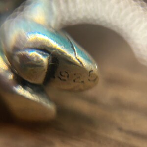 Puede incluir: Primer plano de un amuleto de plata con el n&uacute;mero "925" estampado.