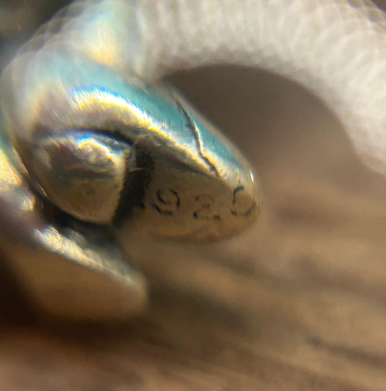 Puede incluir: Primer plano de un amuleto de plata con el n&uacute;mero "925" estampado.