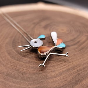 May include: A silver necklace with a colorful bird pendant. The bird is made of turquoise, coral, and mother of pearl. The pendant is attached to a silver chain.