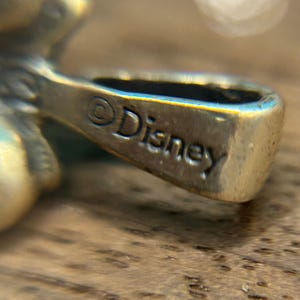 Puede incluir: Primer plano de un amuleto de plata con la palabra "Disney" grabada en la parte posterior.
