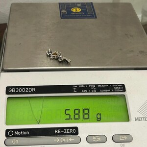 Puede incluir: Un amuleto de plata con una piedra amarilla en forma de tri&aacute;ngulo. El amuleto est&aacute; en una b&aacute;scula que marca 5,88 gramos.