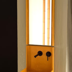 May include: A yellow concrete sink with two black faucets and a mirror above it. The mirror is framed in wood and reflects two bamboo stalks.