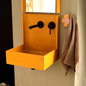 May include: A yellow concrete bathroom sink with a black faucet and a towel hanging on a hook.