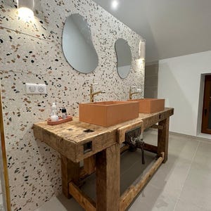Peut inclure: Un plan de travail en bois rustique avec deux lavabos en terre cuite et des robinets dorés. Le mur derrière l'évier est recouvert de carreaux de terrazzo de différentes couleurs et tailles. Deux miroirs ovales sont accrochés au mur au-dessus des lavabos.