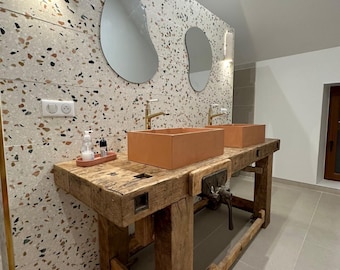 Könnte beinhalten: Ein Badezimmerwaschtisch bestehend aus einer umfunktionierten Werkbank aus Holz mit einem Metallschraubstock, zwei rechteckigen terrakottafarbenen Waschbecken, goldfarbenen Armaturen und zwei unregelmäßig geformten Spiegeln an einer Terrazzowand.