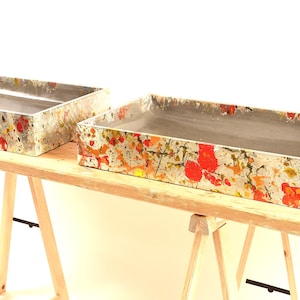 Peut inclure: Deux jardinières rectangulaires en béton avec un design abstrait coloré. Les jardinières sont posées sur des chevalets en bois.