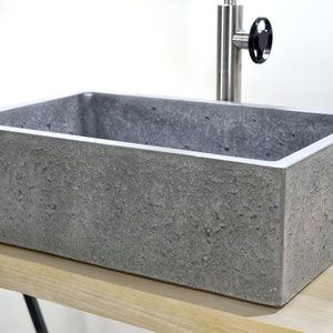 May include: A rectangular concrete sink with a rough, textured surface. The sink is grey and is sitting on a wooden countertop.