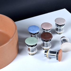 Puede incluir: Un juego de ocho tapones de desagüe de lavabo de cerámica en varios colores, incluyendo azul, verde, marrón, rosa y blanco. Los tapones están hechos de cerámica y tienen un acabado cromado.