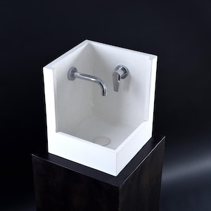 May include: A white square sink with a chrome faucet and a chrome drain stopper. The sink is mounted on a black pedestal.