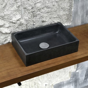 May include: A black rectangular bathroom sink with a drain stopper, sitting on a wooden countertop.