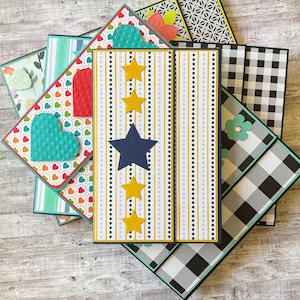 May include: A stack of colorful cards with different patterns, including hearts, stars, and stripes. The cards are decorated with blue, red, yellow, and white accents.
