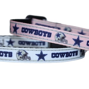 May include: Two Dallas Cowboys pet collars, one pink and one white, with the team logo and the word "COWBOYS" repeated on each.