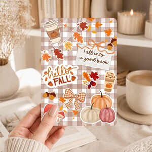 May include: A rectangular card featuring a brown and white gingham pattern decorated with autumn-themed stickers including pumpkins, fall leaves, acorns, coffee cups, a bow, and a note with the text Fall into a good book and hello FALL.
