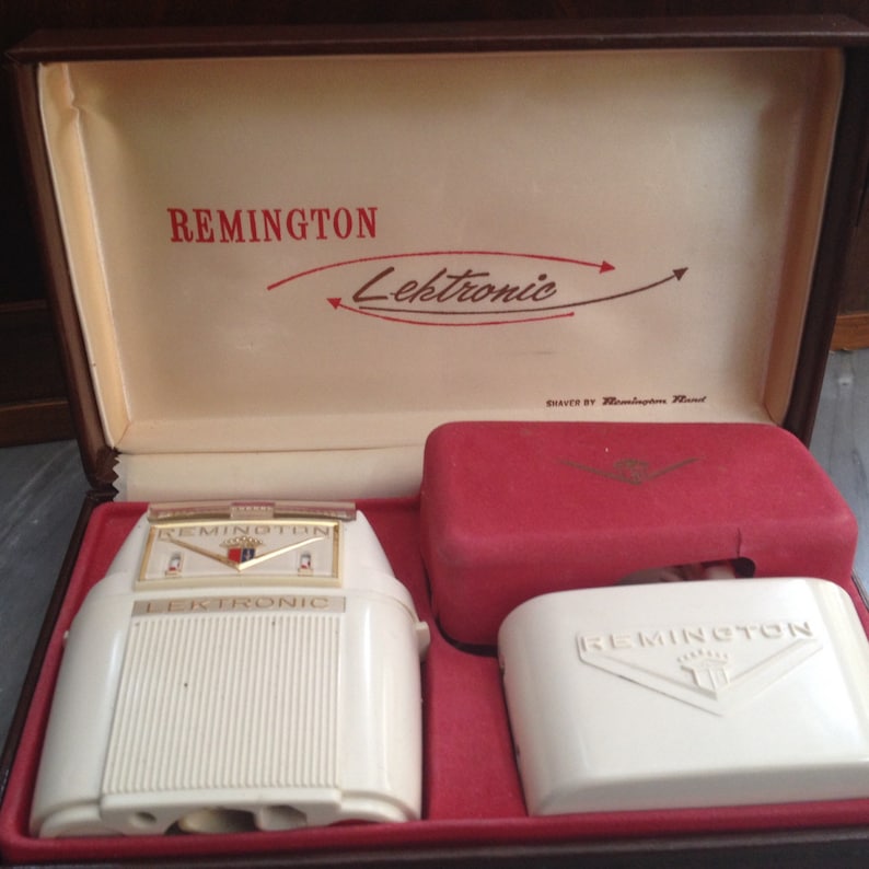 May include: A white electric razor in its original box. The box is brown with a white interior and the words "Remington Lektronic" printed in red. The razor has a white plastic body with gold accents and the words "Remington Lektronic" printed on the front.