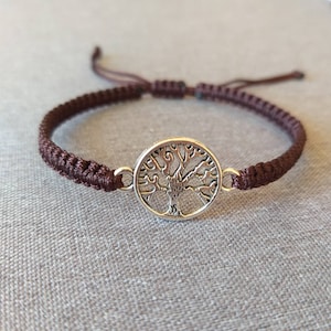 May include: A brown braided cord bracelet with a silver tree of life charm.