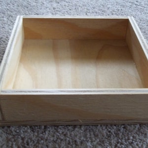 May include: A plain wooden box with a rectangular shape. The box is made of light-colored wood and has a smooth surface.