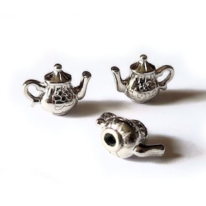 May include: Three silver teapot charms with intricate details. The charms are small and delicate, perfect for adding a touch of whimsy to a bracelet or necklace.