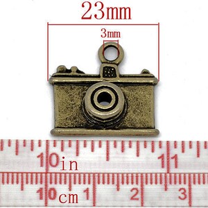 May include: A gold-toned metal camera charm with a 3mm loop at the top. The charm measures 23mm in length.