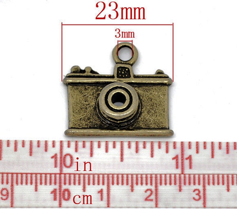 May include: A gold-toned metal camera charm with a 3mm loop at the top. The charm measures 23mm in length.