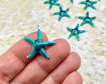 May include: Teal starfish charms with silver-colored loops for jewelry making. The starfish have a metallic finish with dark blue accents. The charms are small and have a detailed design, perfect for creating ocean-themed accessories.