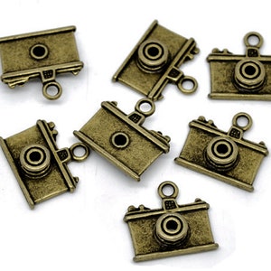 May include: Seven antique gold-toned camera charms with a loop for hanging. The charms are detailed with a lens and other camera features.