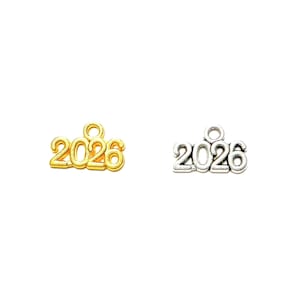 May include: Two metal charms, one gold-toned and one silver-toned, each displaying the year "2026". The charms have a small loop at the top for attaching to jewelry or other crafts. The numbers are in a simple, clear font.