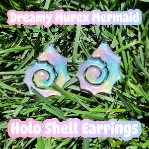 May include: A pair of spiral-shaped shell earrings featuring a holographic finish with iridescent swirls of pink, blue, and purple. The text Dreamy Murex Mermaid Holo Shell Earrings is displayed in white letters with a soft pink and blue gradient background.