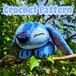 May include: A blue and white crochet plush toy of a cartoon character with large ears, resting on a tree branch. The text "Crochet Pattern" is displayed in a light blue font at the top of the image. The plush has a dark blue nose and black eyes.