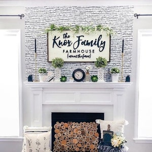May include: A white fireplace mantel with a black and white patterned wallpaper behind it. The mantel is decorated with a wooden sign that reads "The Knox Family Farmhouse (minus the farm)", greenery, and a clock. The fireplace has a black metal grate with a wood log fire screen.