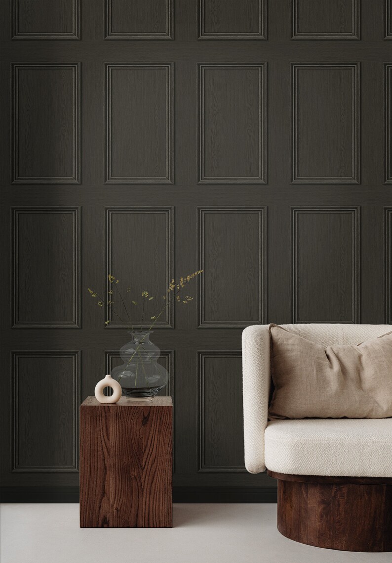 Op de afbeelding: Een donkergrijze houten lambrisering met een witte bank en een houten bijzettafel met een vaas met gedroogde bloemen. De bank heeft een beige kussen en een houten onderstel.
