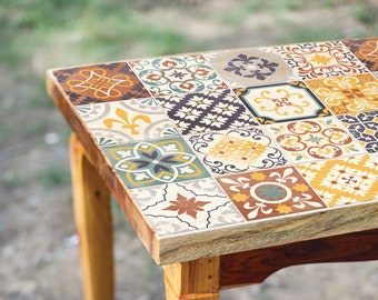 May include: A wooden table with a decorative tile top. The tiles are in various shades of brown, yellow, blue, and green. The table has a rustic, farmhouse style.