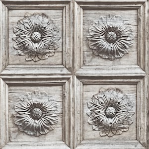 Pode incluir: Um close-up de um painel de madeira com quatro desenhos florais esculpidos. O painel é pintado de cinza claro e tem um aspecto envelhecido.